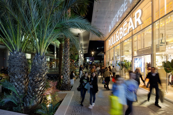 Customers stroll at nightfall in Polygone Riveria, past the store Pull&Bear